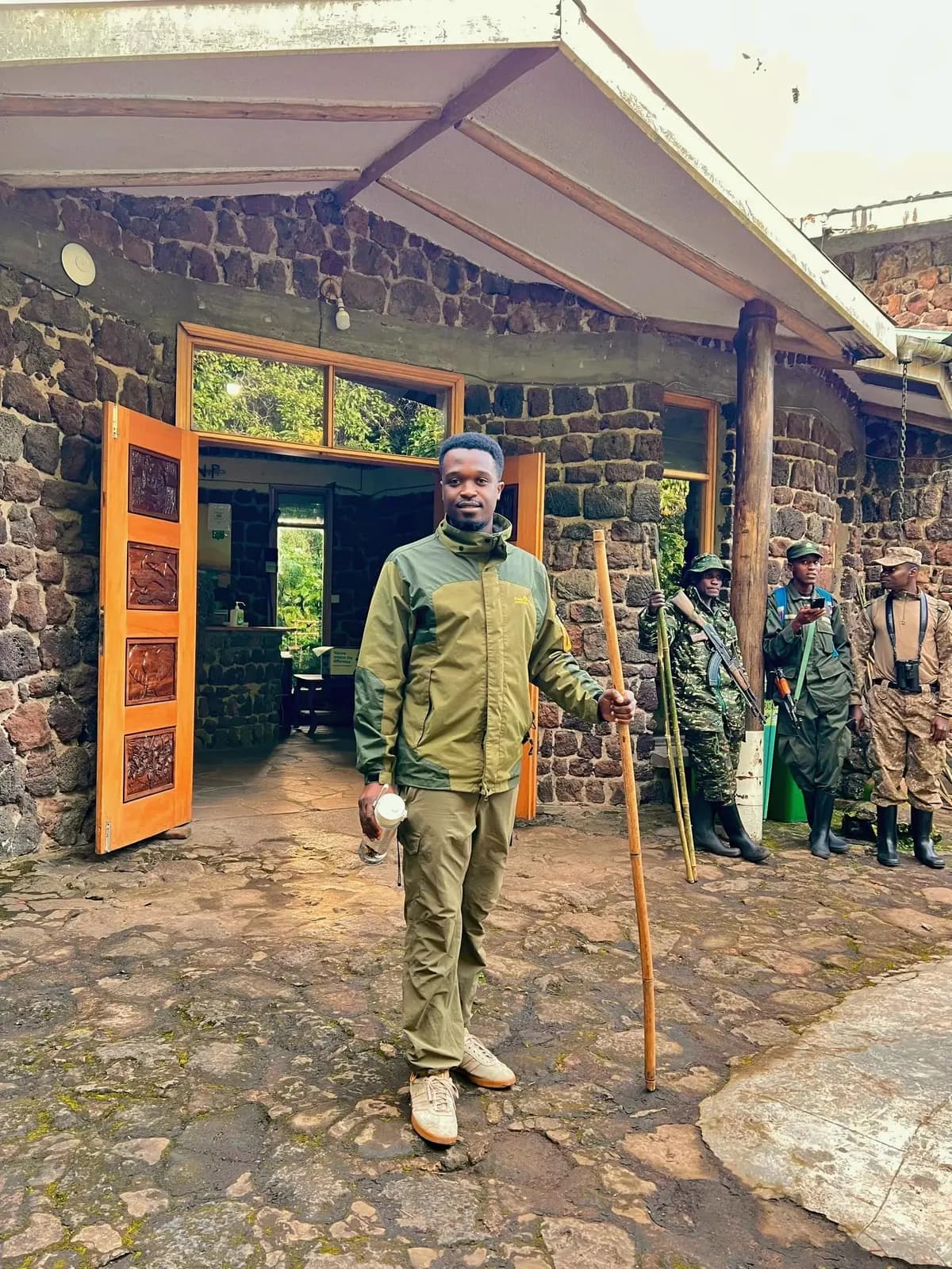 Guide standing outside a stone ranger station with trekking staff nearby